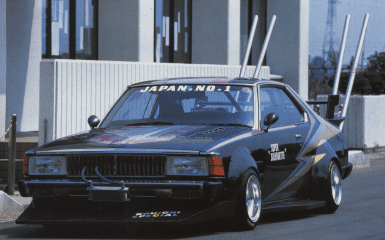 Modified vintage Japanese race car with custom decals and tall exhaust pipes, parked in front of a modern building.
