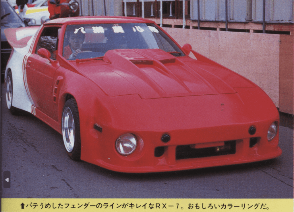 Vintage red Mazda RX-7 with custom widebody kit and bold styling on city street.