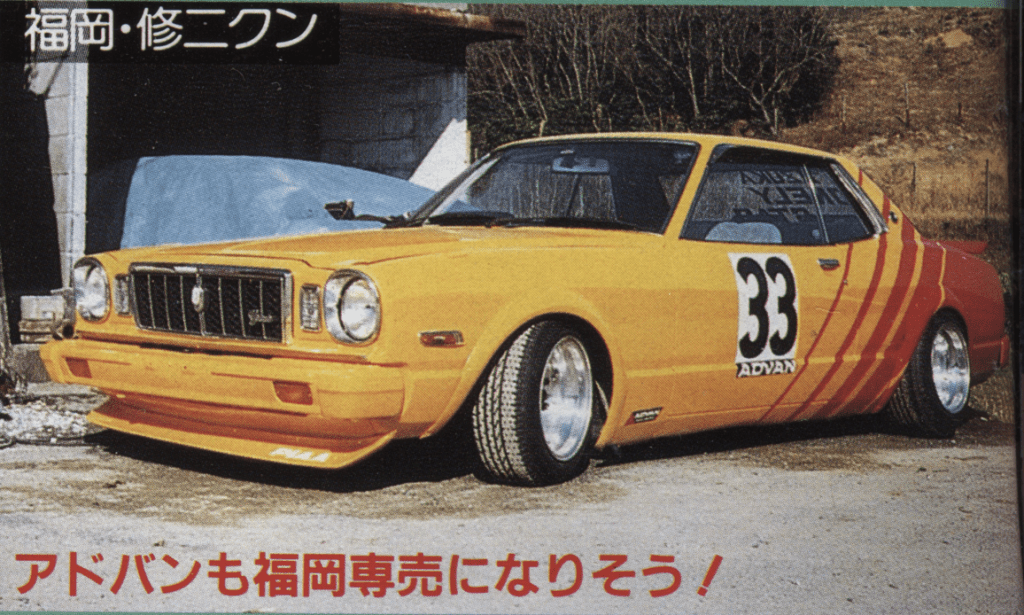 Vintage yellow race car with number 33 and Advans logo parked near a garage.