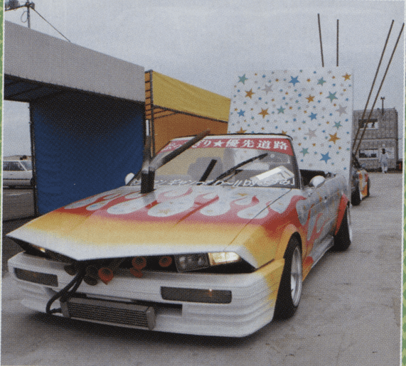 Colorful custom car with flame design and star backdrop at a car show.
