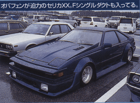 Modified blue Toyota Celica XX parked in a lot on a rainy day, showcasing aerodynamic body kit and custom wheels.
