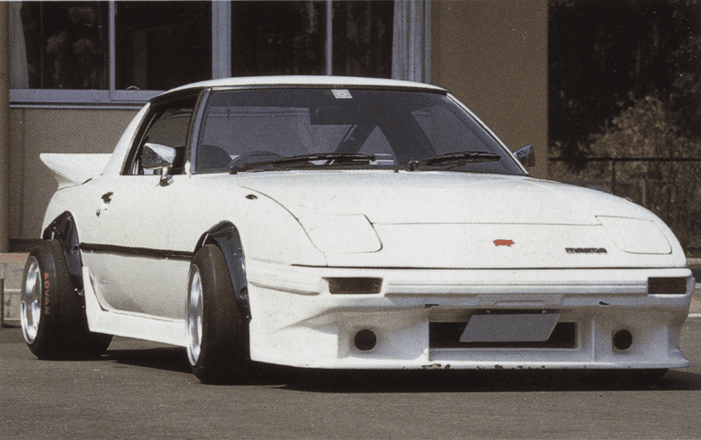 White sports car with wide body kit and spoiler, parked outside a building.
