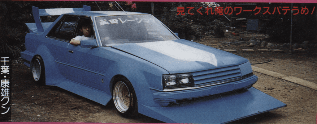 Modified blue car with a large front spoiler and unique styling, parked outdoors.