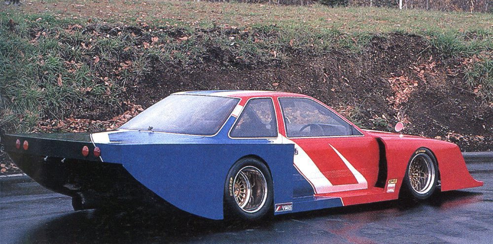 Vintage red, white, and blue racing car on a wet road, showcasing aerodynamic design and wide rear spoiler.
