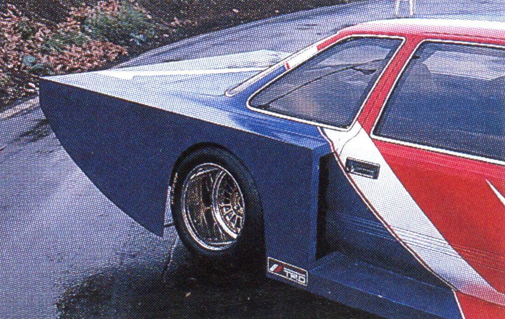 Futuristic custom car with striking geometric design and bright red, white, and blue paint on a wet road.