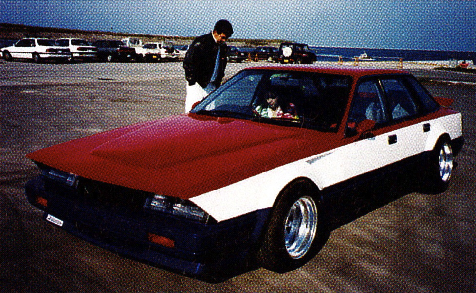 Red and white retro car on a seaside parking lot, with a person standing beside it.