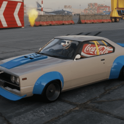 Modified vintage car with Coca-Cola banner on the side at an industrial area, painted in blue and white.