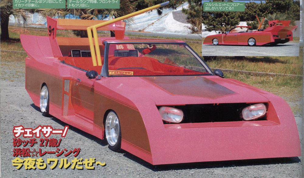 Unique modified car with vibrant pink body and large spoiler, parked outdoors on a sunny day.
