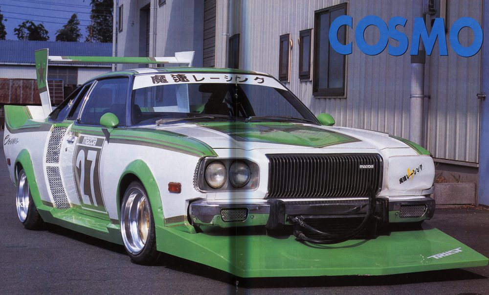 Vintage Mazda Cosmo race car with custom green and white design parked outside a garage.