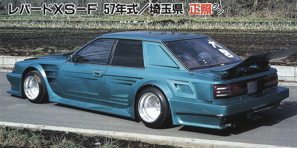 Modified turquoise sports car with custom body kit and spoiler parked on a street.