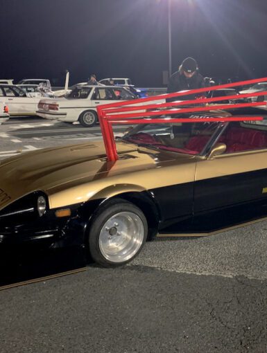 Custom vintage Nissan sports car at night car meet, featuring distinctive body modifications and bold styling.