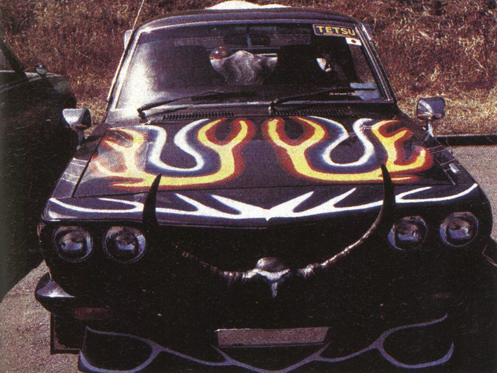 Vintage car with flame decals and bullhorns, showcasing custom art and design on the hood.
