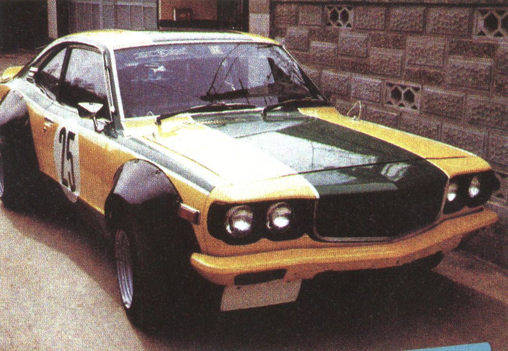 Vintage yellow and green Mazda race car parked in front of a stone wall, displaying number 25 on the door.
