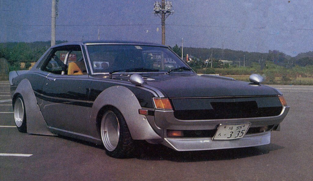 Vintage modified car with wide fenders on a parking lot, showcasing a retro Japanese design.