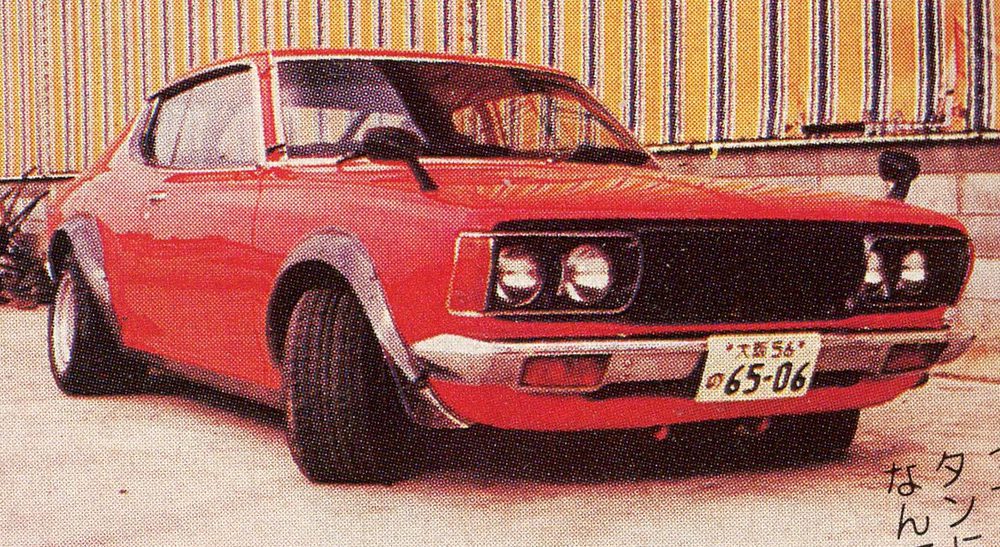 Vintage red car with Japanese license plate, parked in front of a striped building.