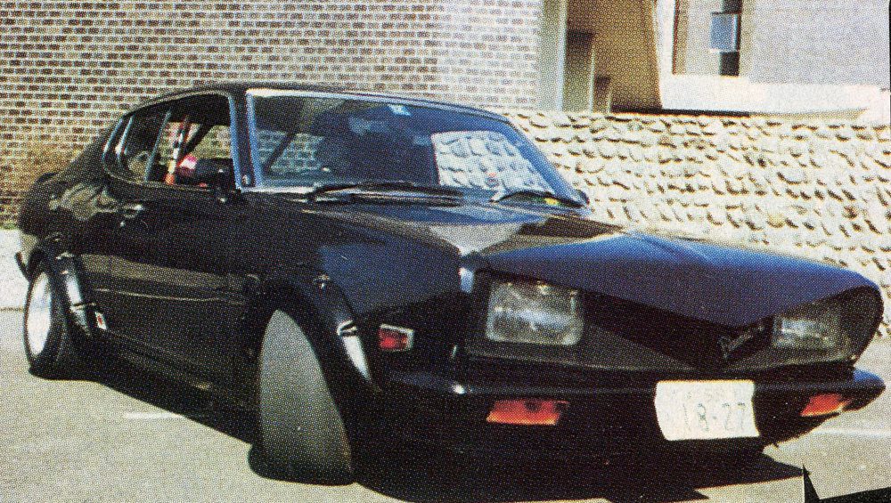 Vintage black sports car parked, side view showcasing sleek design against brick wall background.
