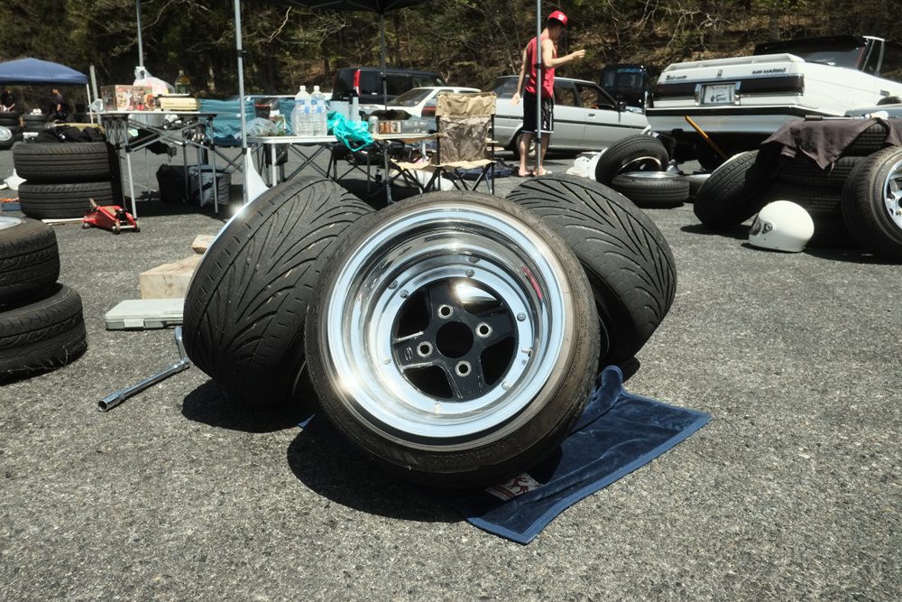 Stack of Super Star Racing Mark II wheels and performance car tires on display at an outdoor auto event with cars and equipment in the background.
