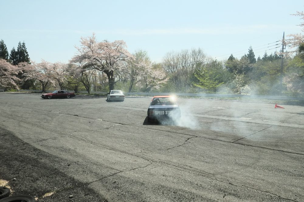 Car drifting on track with cherry blossom trees in the background, creating smoke and action.