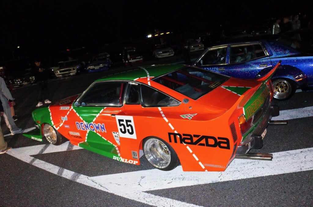 Customized Mazda Cosmo race car with vibrant Renown livery, number 55, displayed at night event.