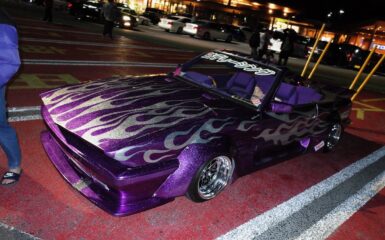 Customized purple car with flame decals in a parking lot at night.