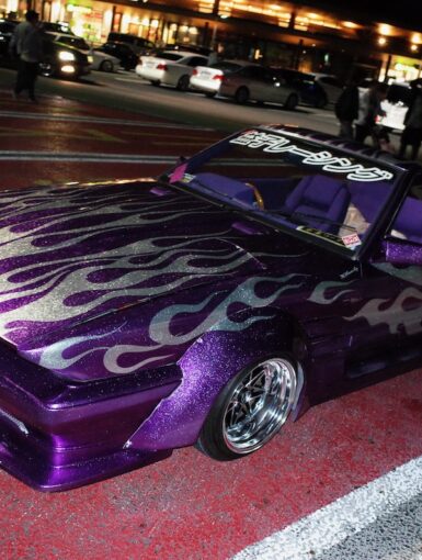 Customized purple car with flame decals in a parking lot at night.