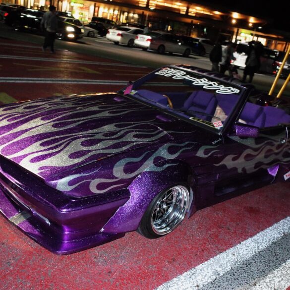 Customized purple car with flame decals in a parking lot at night.