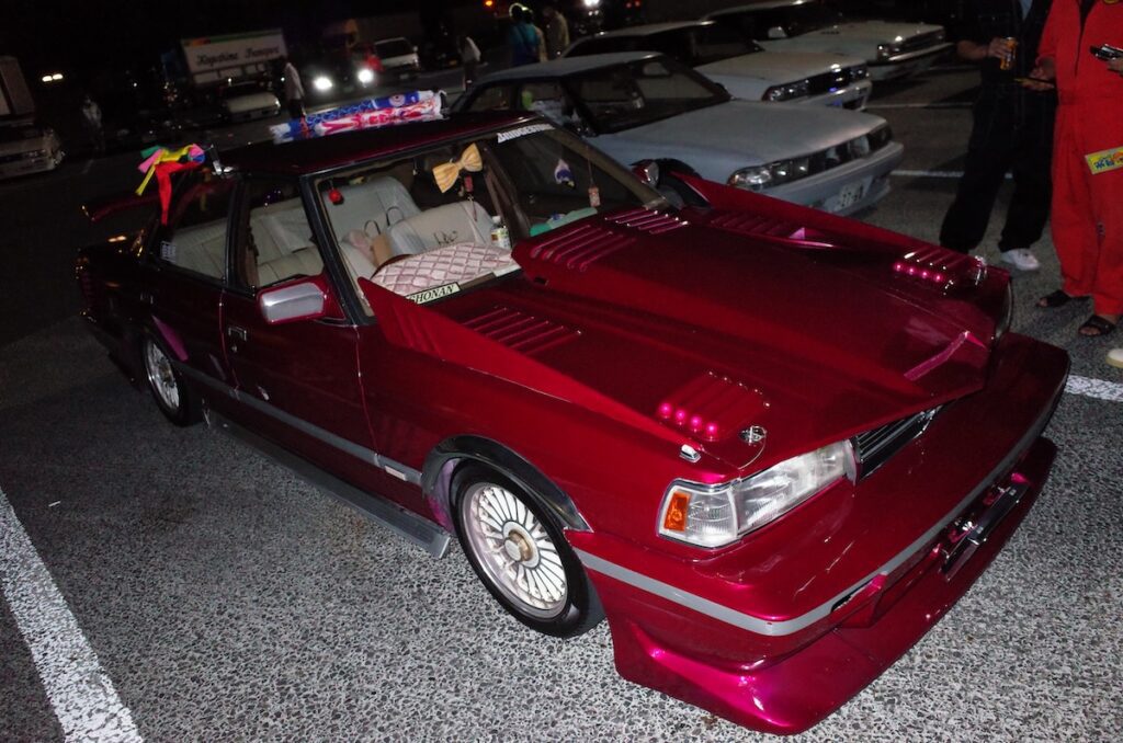 Custom red car with unique body kit and colorful decorations at night car meet.