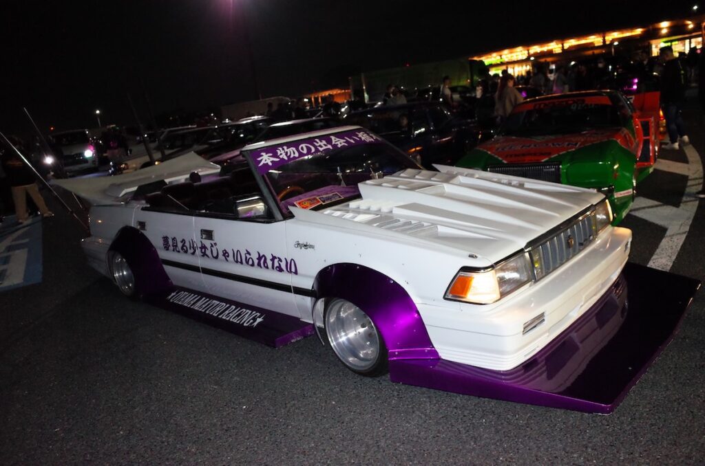 Modified car with custom wide body kit and colorful decals at night car meet.