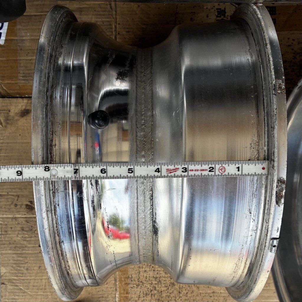 Close-up of a metallic car rim with visible ruler for diameter measurement on a wooden surface.