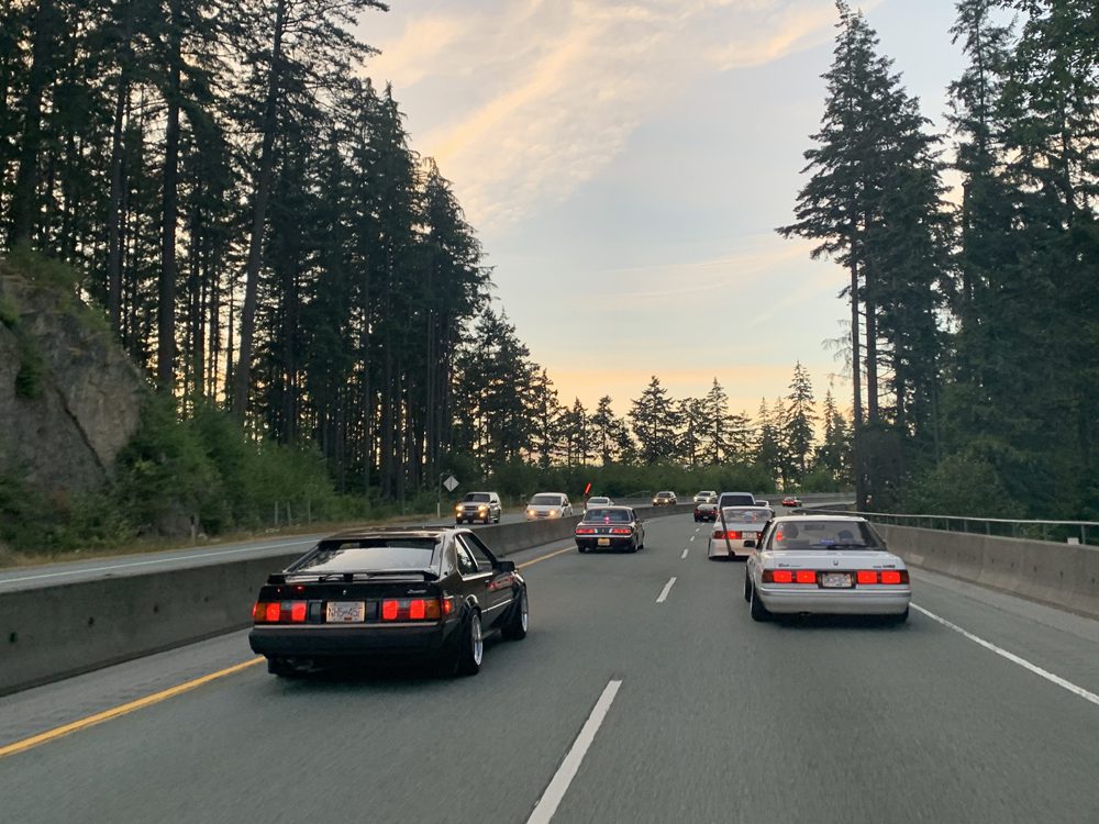 Cars driving on a scenic highway through a forested area at sunset.