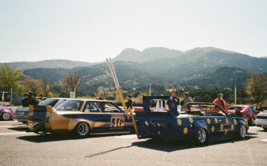 Vintage Japanese cars at a car meet with mountain backdrop and clear skies.