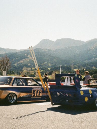 Vintage Japanese cars at a car meet with mountain backdrop and clear skies.