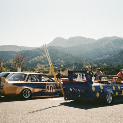 Vintage Japanese cars at a car meet with mountain backdrop and clear skies.