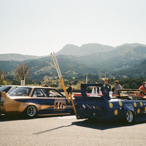 Vintage Japanese cars at a car meet with mountain backdrop and clear skies.