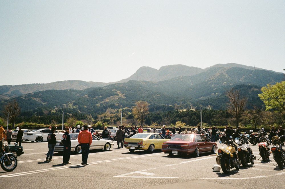 Vintage car and motorcycle gathering in scenic mountain parking lot under clear skies.