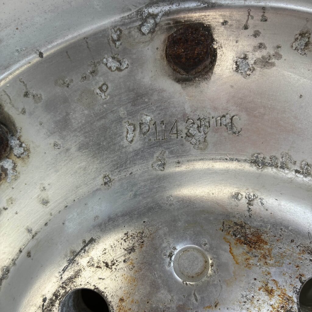 Close-up of a weathered metal wheel rim with rust spots and engraved text P 114.3 MC.