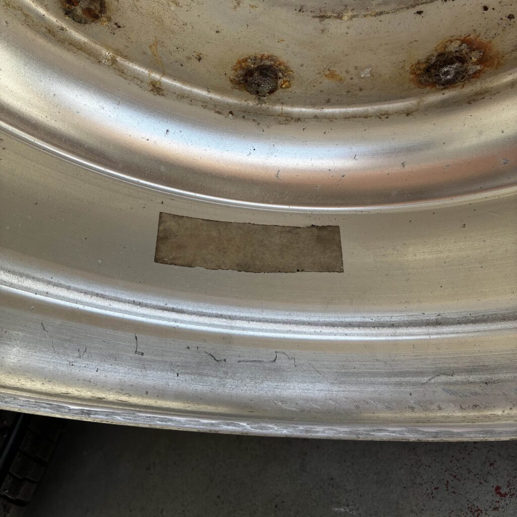 Close-up of a worn metallic wheel rim with visible rust and scratches, showcasing texture and condition.