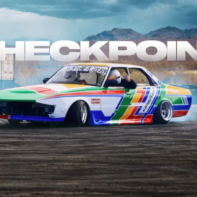 Colorful drift car with driver in helmet sliding on track, CHECKPOINT text in background.