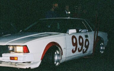 Vintage race car with number 999 painted on the side in a dark setting, showcasing classic design and headlights on.