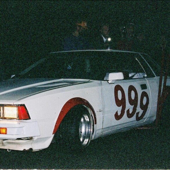 Vintage race car with number 999 painted on the side in a dark setting, showcasing classic design and headlights on.