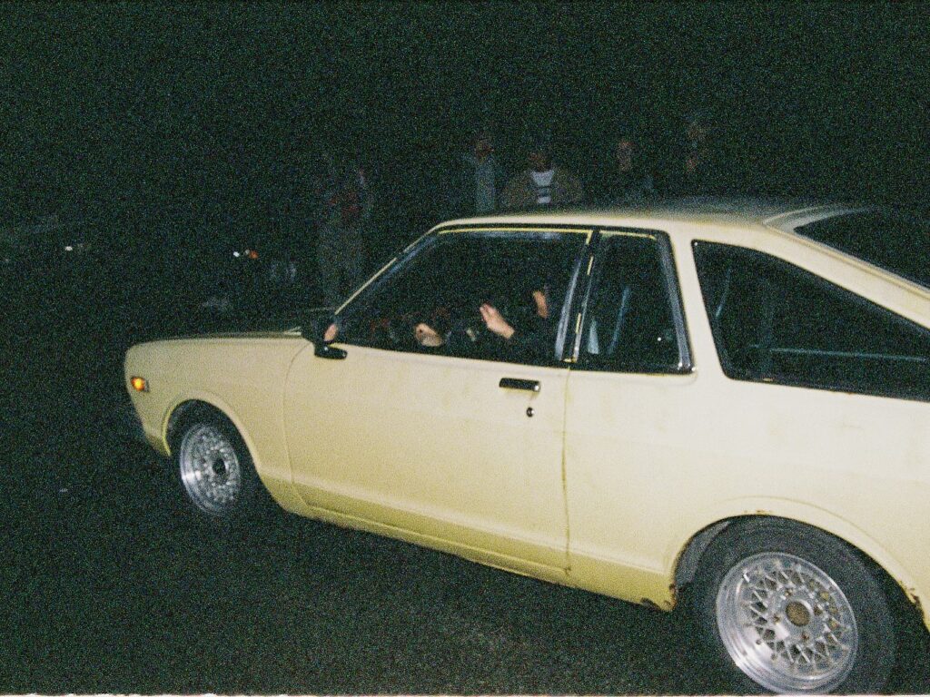 Vintage yellow car with custom rims driving at night.