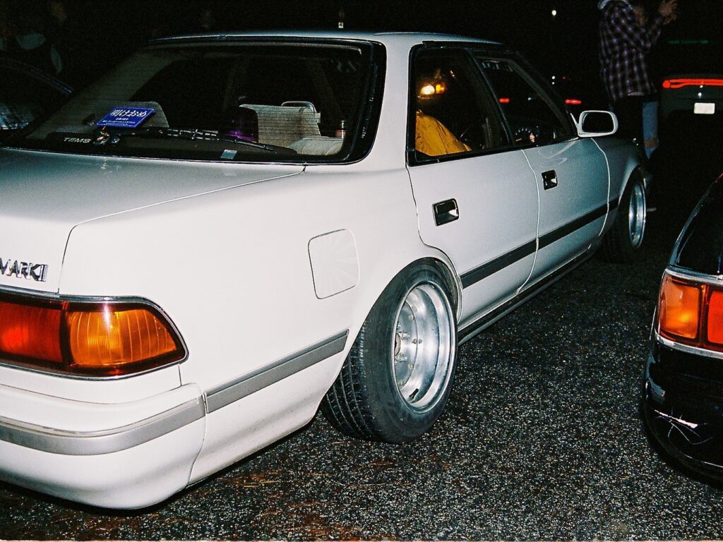 White vintage car with wide tires parked at night, featuring distinctive rear lights and badge.