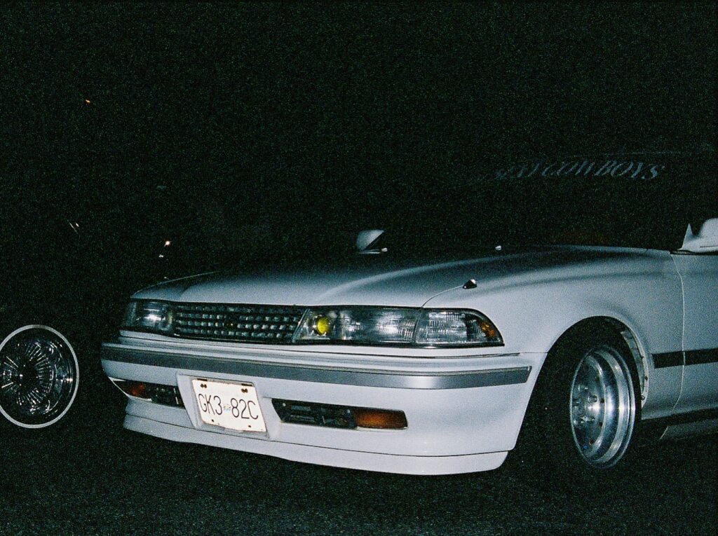 White classic car with custom wheels and a front bumper, captured at night.