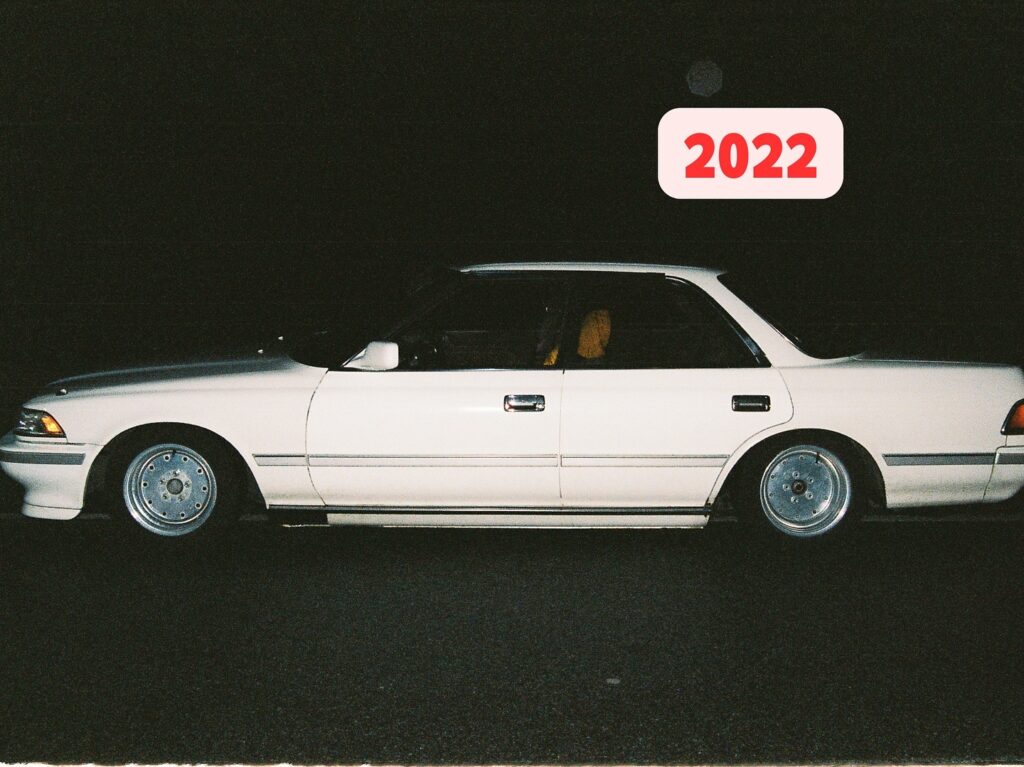 White vintage car from the 90s parked at night, text overlay says 2022.