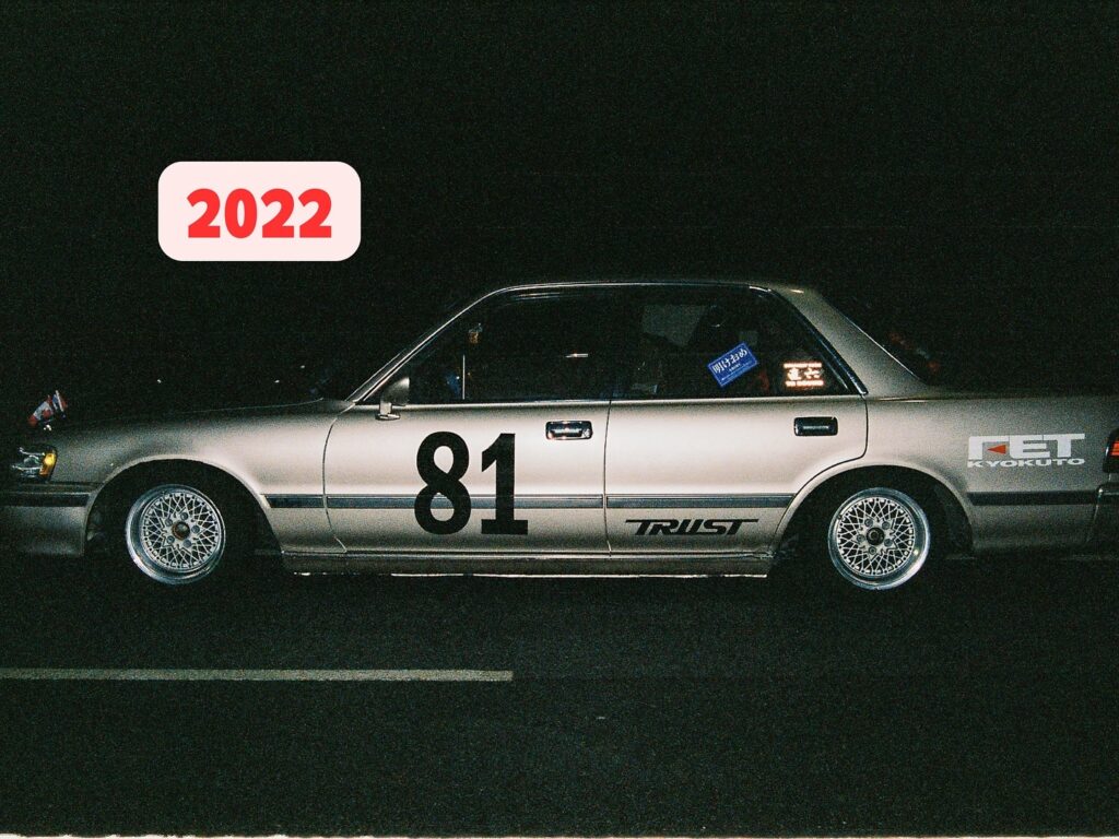 Silver car with the number 81 and various decals, parked at night with a 2022 label above.