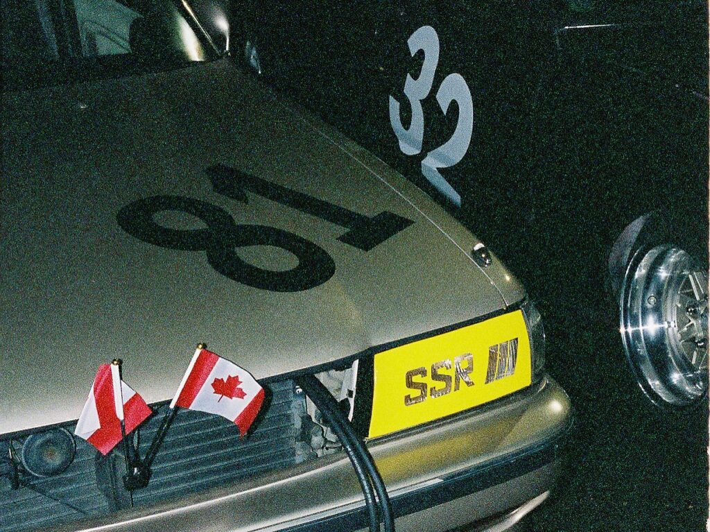 Close-up of a vintage car with number 81, Canadian and Polish flags, and SSR badge on bumper.