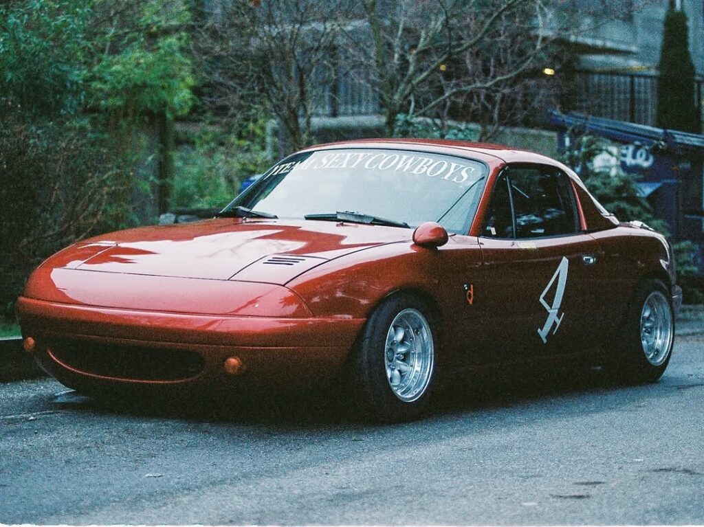 Red sports car with Team Sexy Cowboys decal and number 4 parked outdoors.