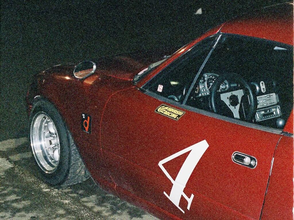 Close-up of a red vintage race car with number 4, featuring a visible steering wheel and racing stickers.