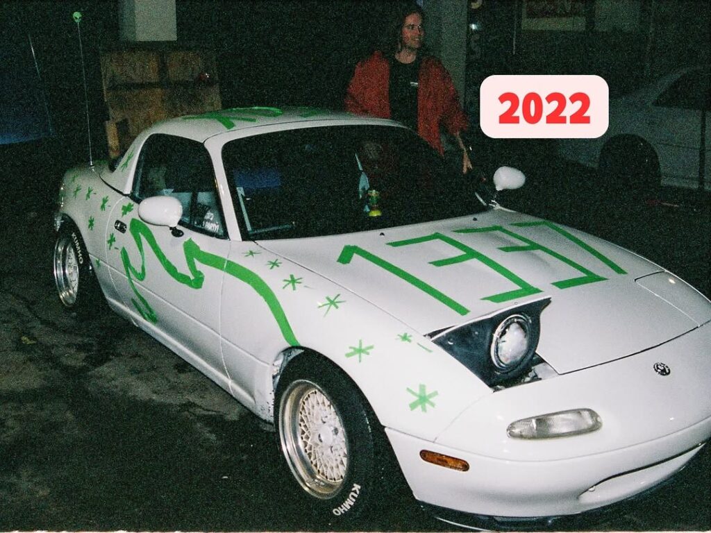 Customized white sports car with green designs and pop-up headlights in a garage, photographed in 2022.