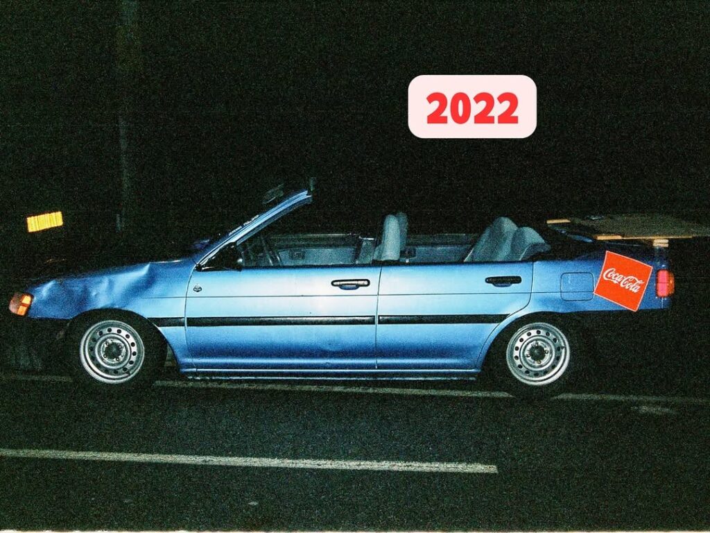 Blue convertible car with a Coca-Cola logo and a 2022 label, parked at night.